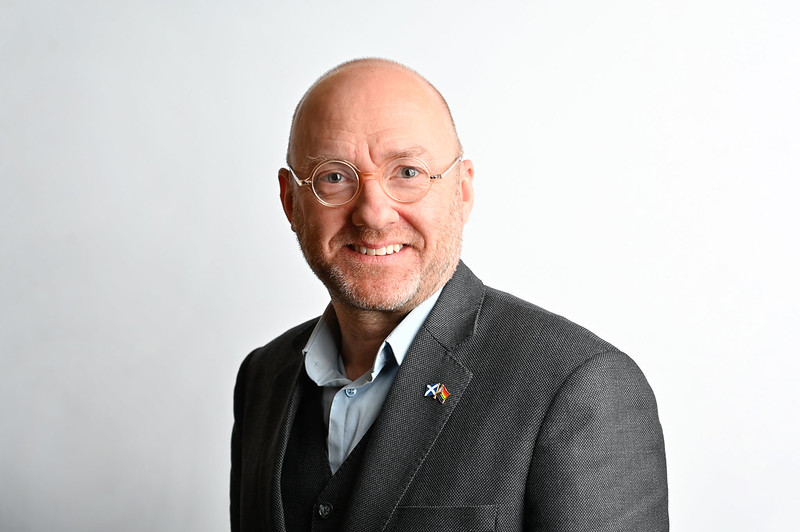 Patrick Harvie facing camera wearing a grey business suit with badge