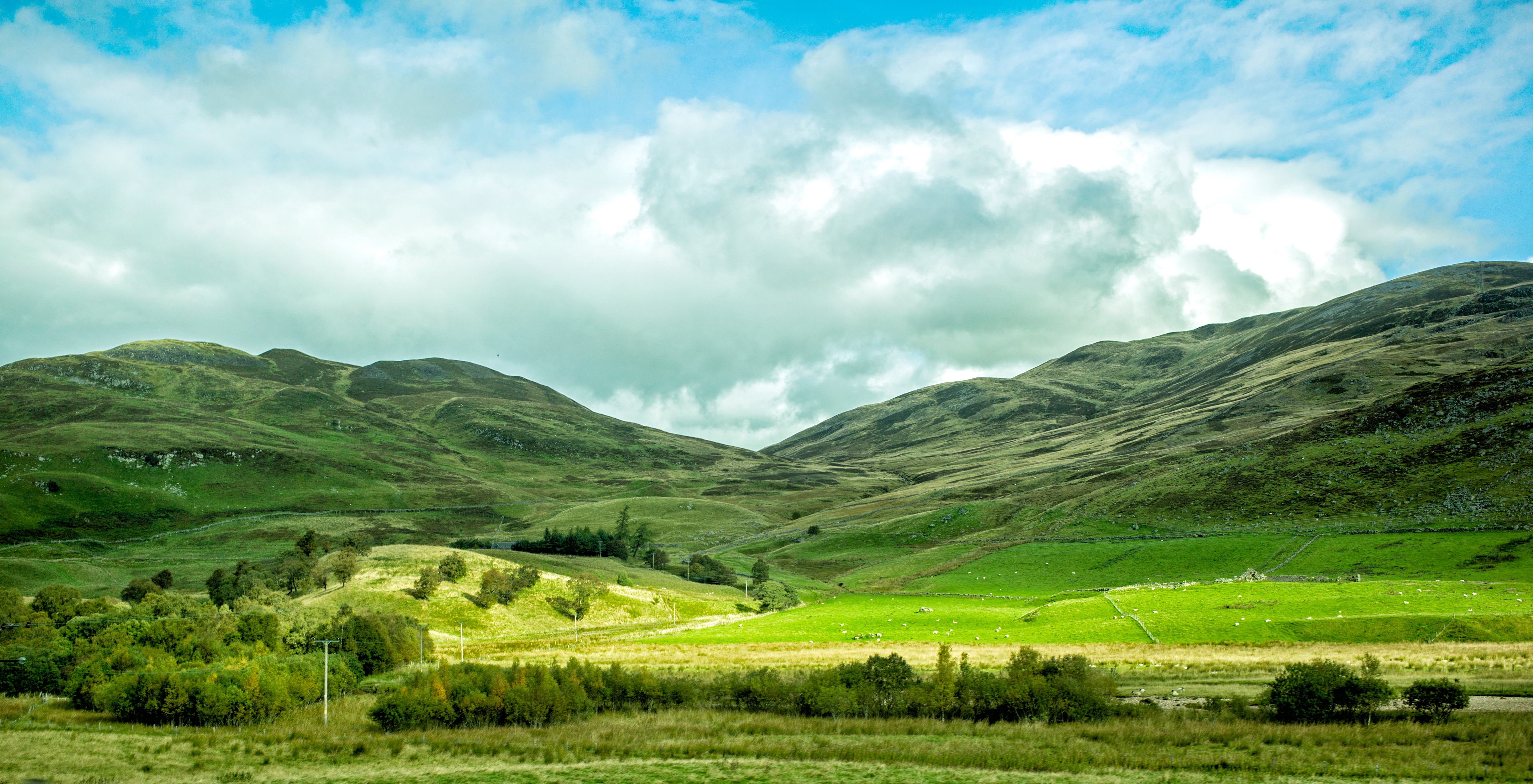 Landscape of Scotland with two green hills and blue sky with clouds.