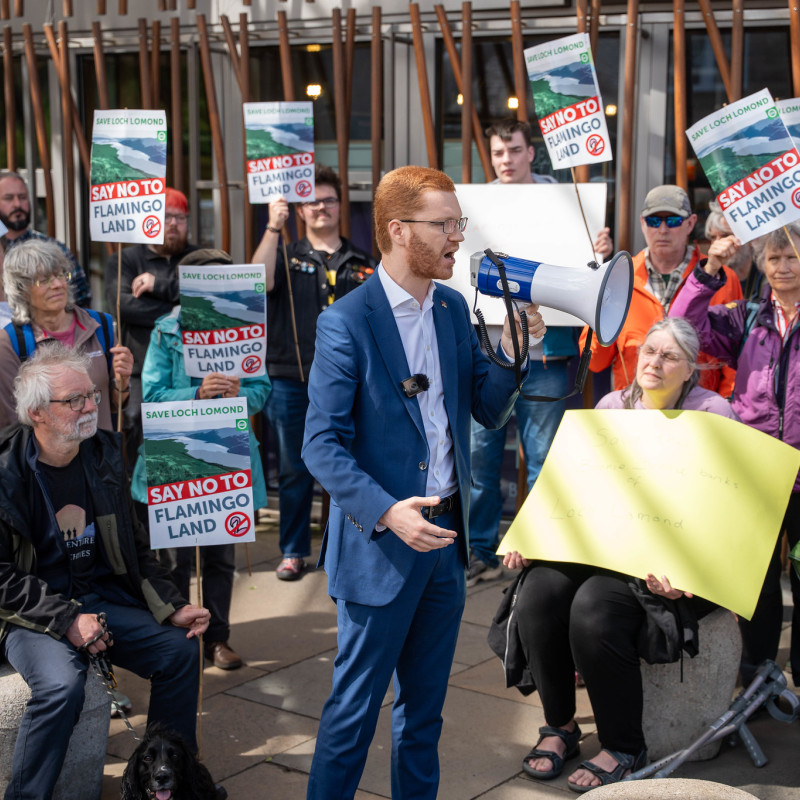Ross Greer MSP speaks in front of a crowd holding Save Loch Lomond signs.