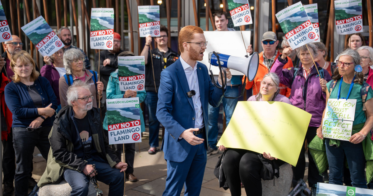 Ross Greer MSP speaks in front of a crowd holding Save Loch Lomond signs.