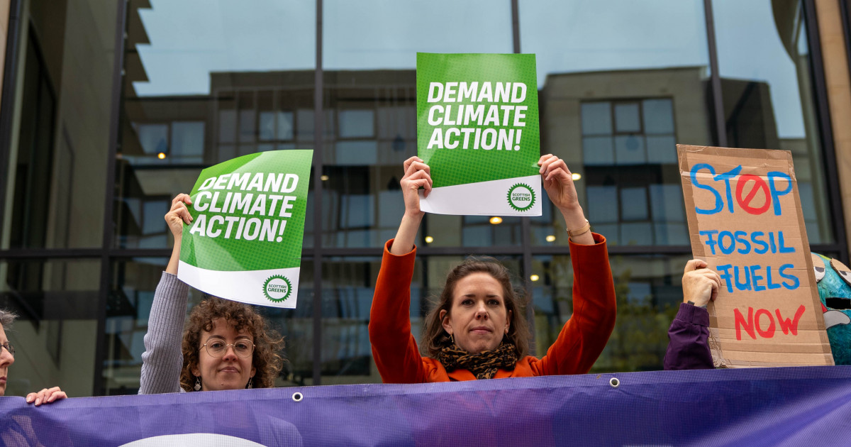 Green Members hold placards outside UK Government building demanding climate action.